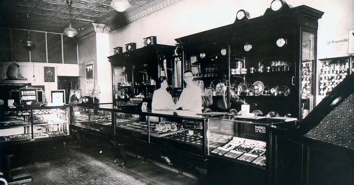 A vintage photograph of the original Vandenberg Jewelers store interior — long glass display cases and wood cabinets of clocks and silver